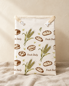 Fresh Daily beeswax bread bag with green wheat and brown loaf print, webbing tabs and side-release clip at the top, standing on linen