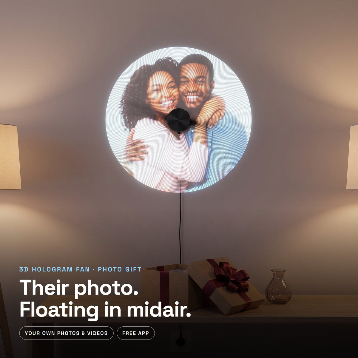 Their photo floating in midair on a wall-mounted hologram fan, with an opened gift below