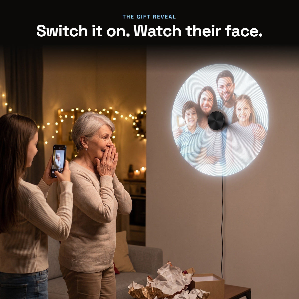 A grandmother reacts as a family photo floats on a hologram fan, her granddaughter films it