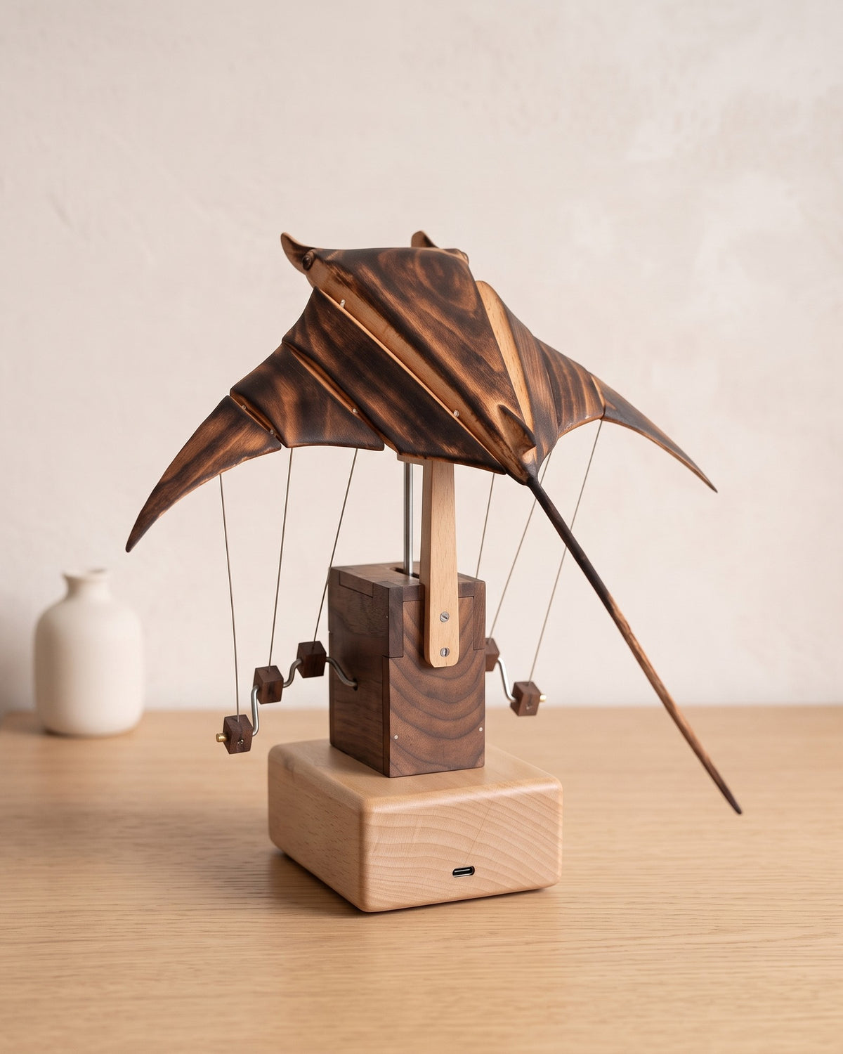 Wooden manta ray sculpture from behind, showing the flame-burnt wings and USB-C base