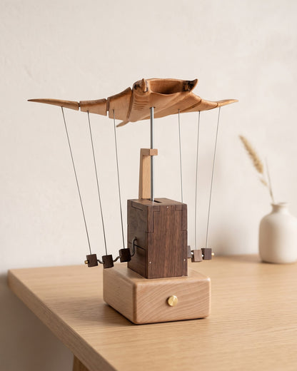 Wooden manta ray kinetic sculpture with wings spread on a light oak table against a warm limewash wall