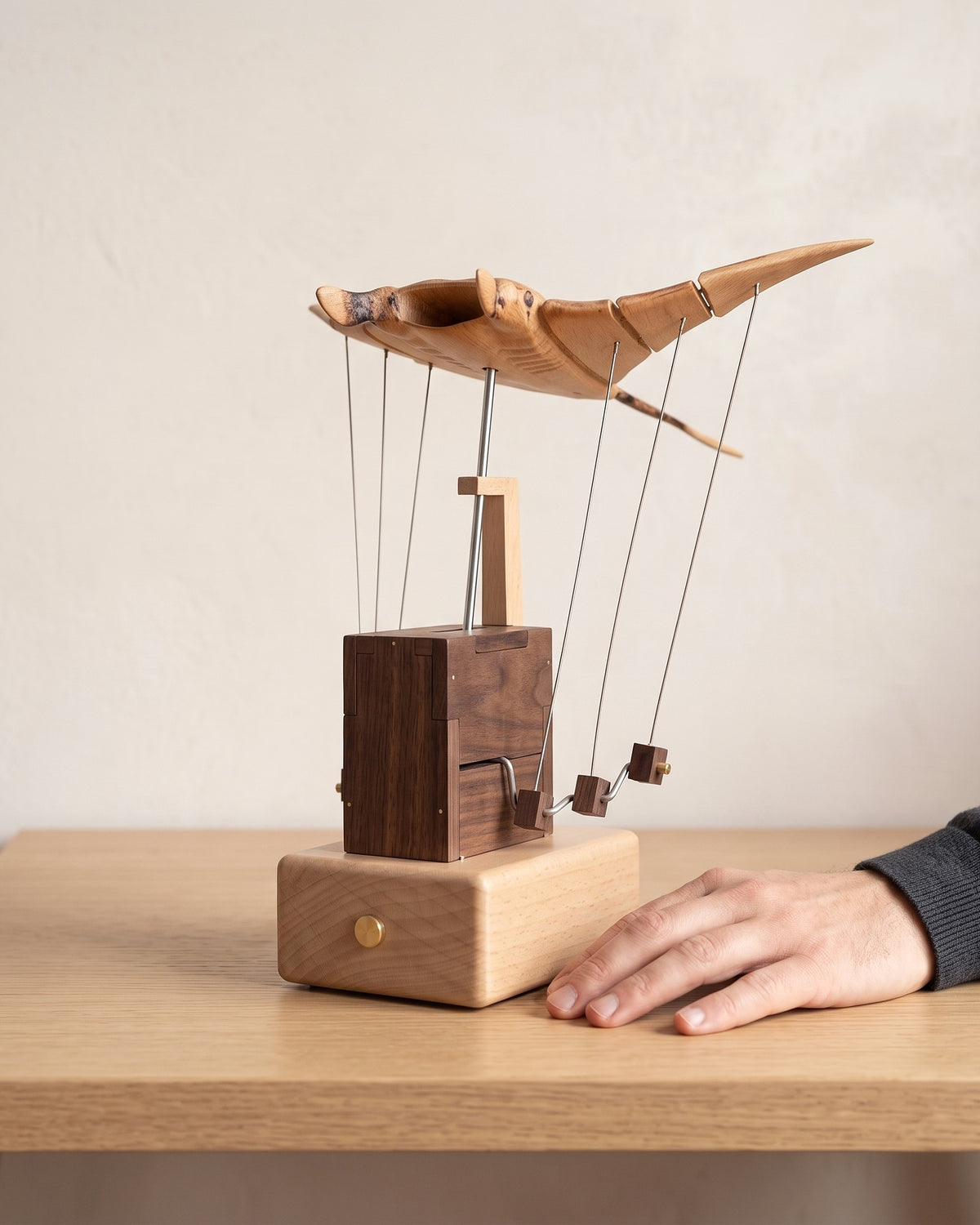 A hand resting next to the wooden manta ray on a table to show its size