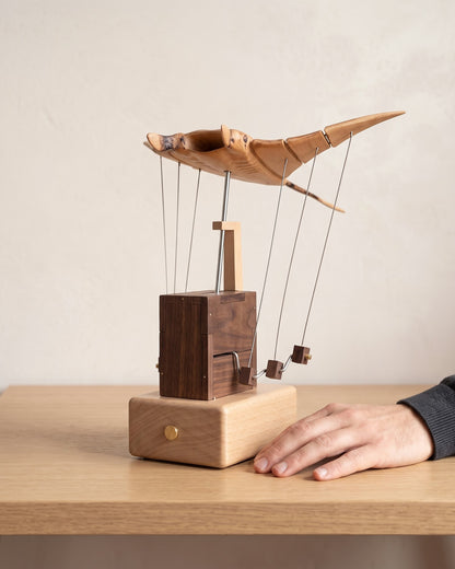 A hand resting next to the wooden manta ray on a table to show its size