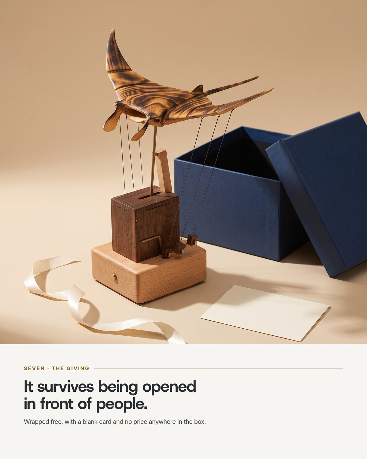 The automaton beside an open navy gift box with cream ribbon