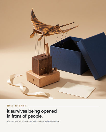 The automaton beside an open navy gift box with cream ribbon