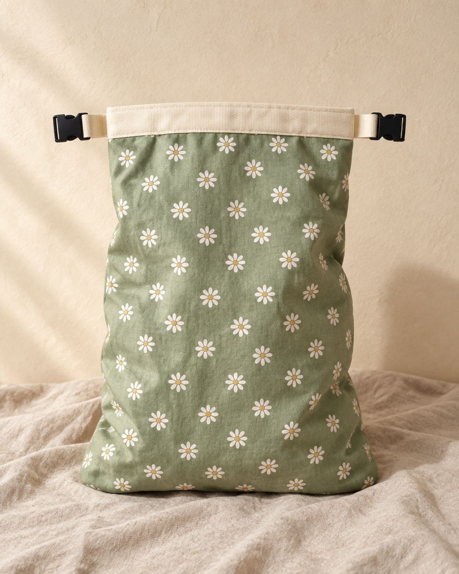 Meadow beeswax bread bag in sage green with white daisies, cream band and black side-release buckles, standing on linen