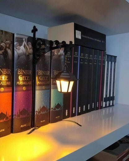 Mini Library Lantern lit on a bookshelf, warm light across the spines