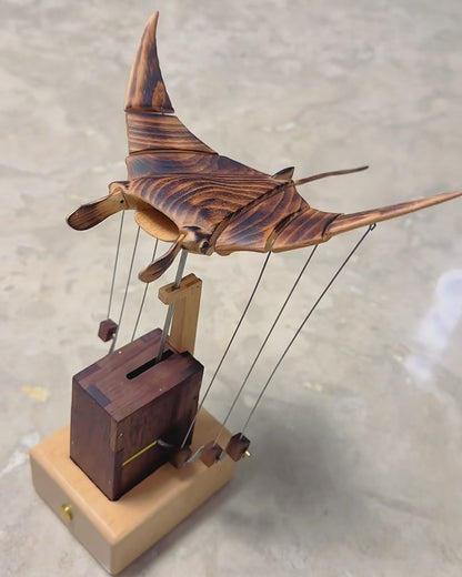 Wooden manta ray beating its wings in soft even daylight, flame-burnt beech grain visible from above